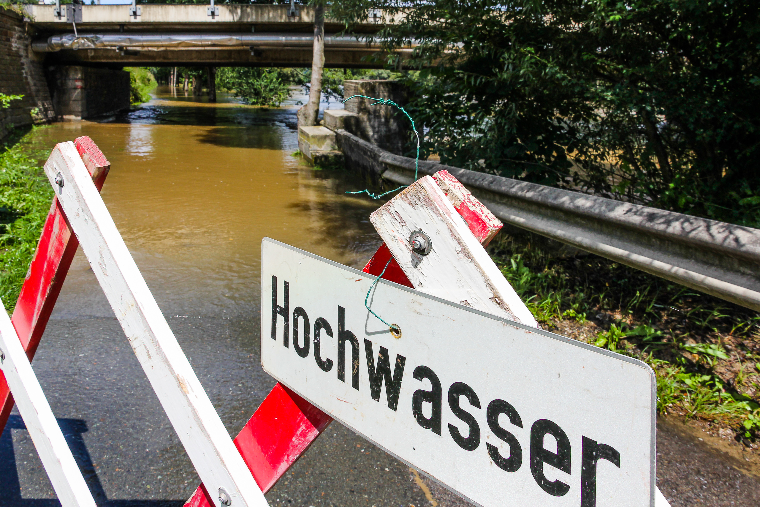 „Hochwasser" – der Murradweg steht braun unter der Brücke, Absperrung quer über den Weg